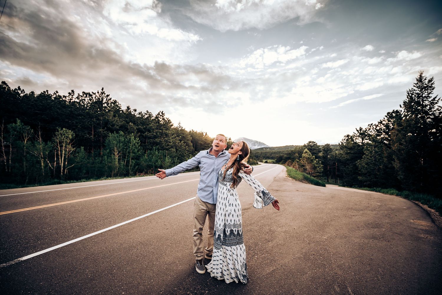 A playful couple dances on an empty mountain road during sunset.