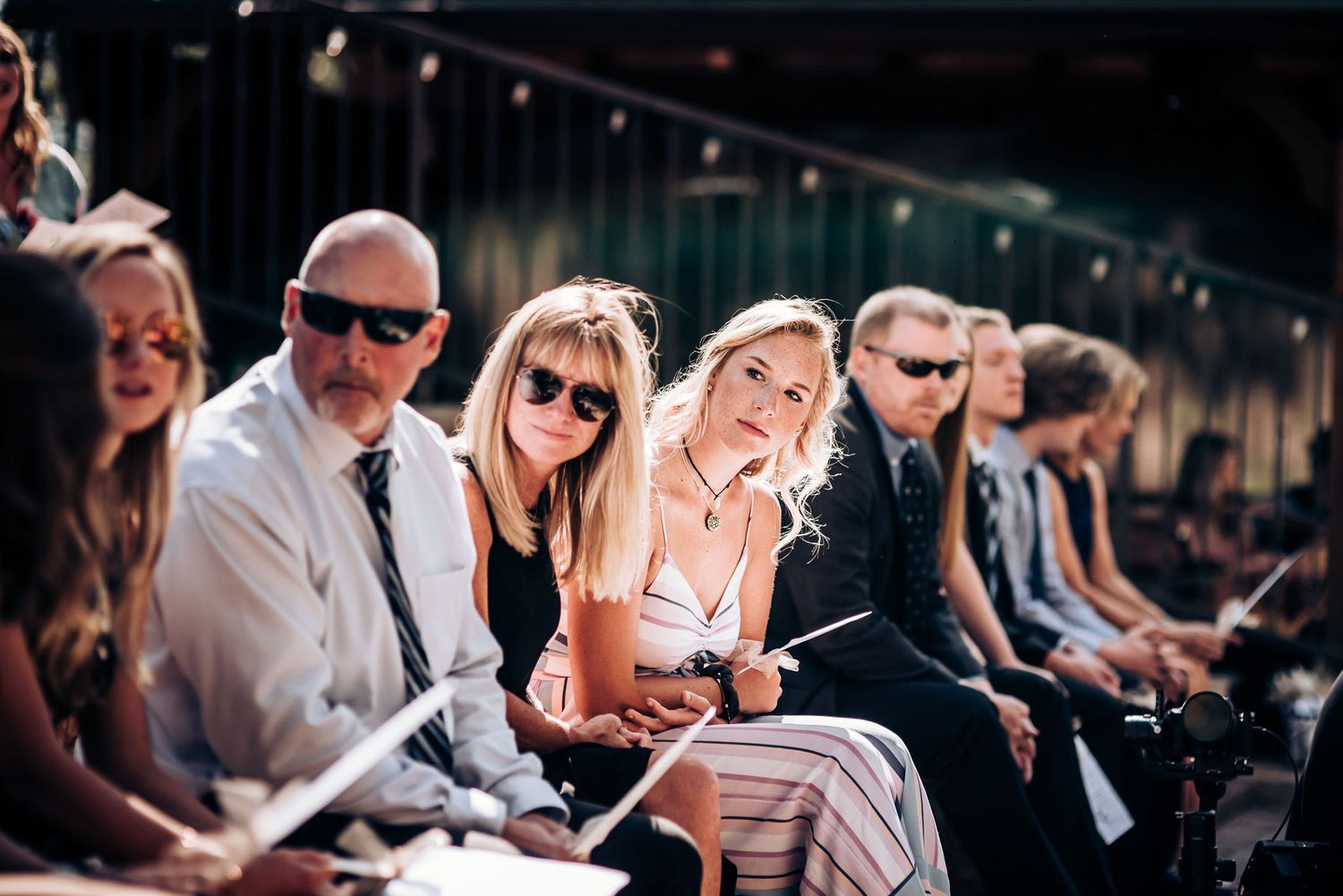 Wedding guests seated on wooden benches during an outdoor ceremony.