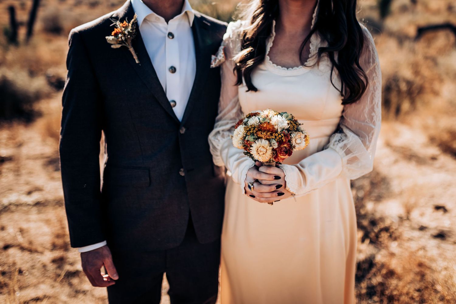 Close up of wedding attire and autumn bouquet against desert backdrop.