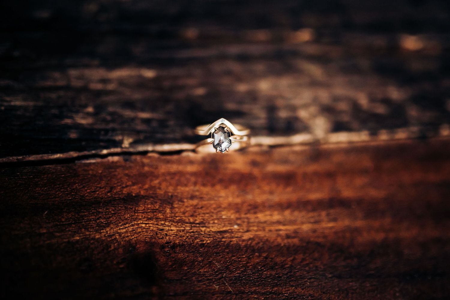 Elegant diamond engagement ring photographed on rustic wooden surface with shallow depth of field.