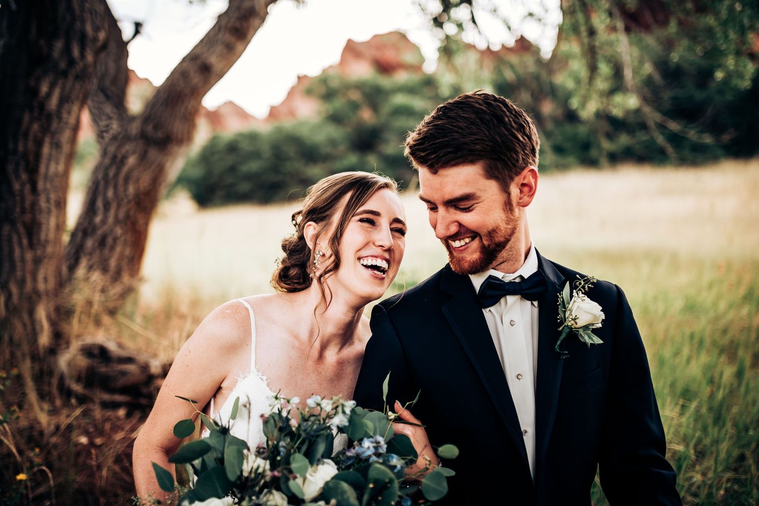Joyful wedding couple shares intimate laugh during outdoor photo session.