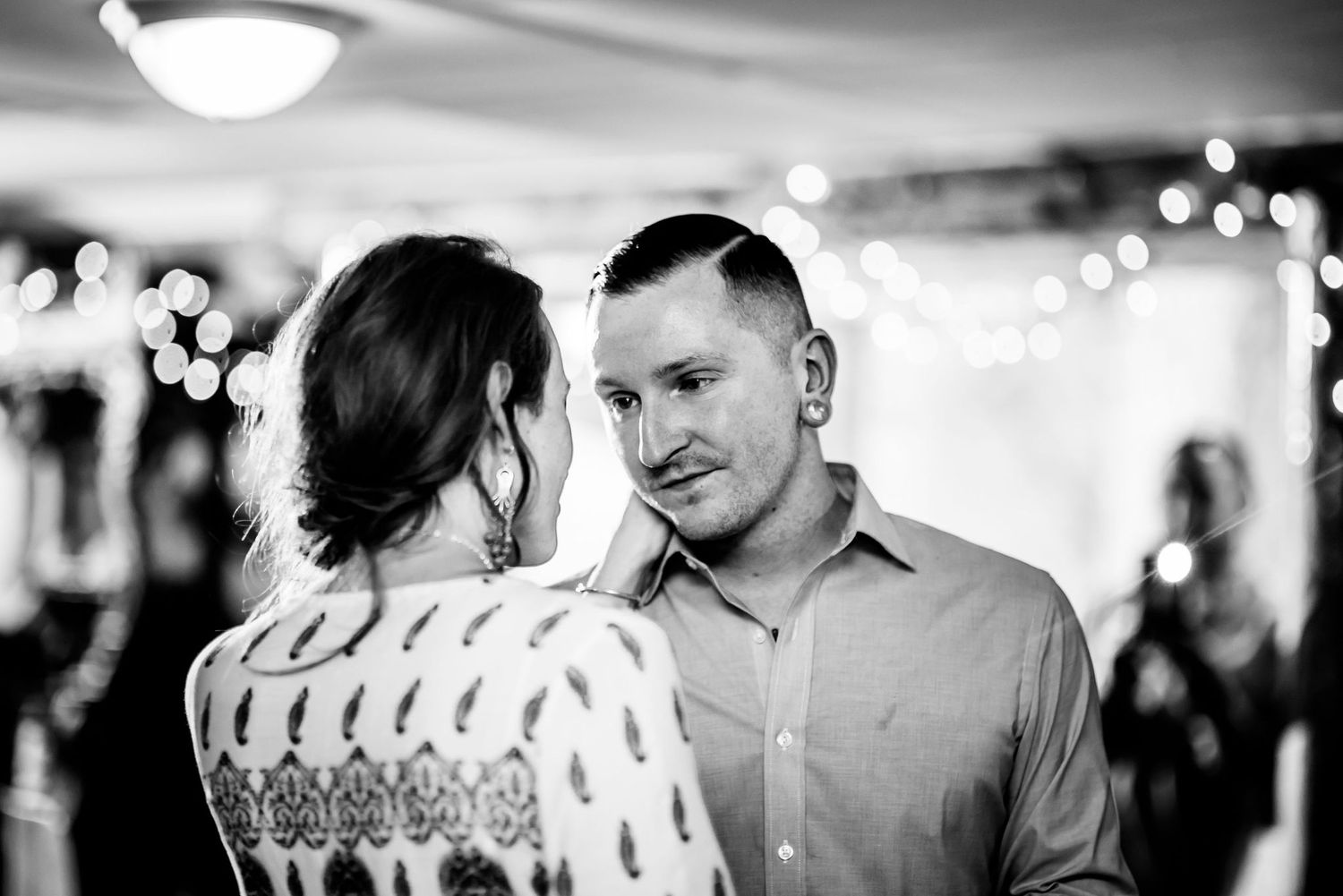 A romantic black and white moment at an indoor celebration with string lights and decorative ambiance.