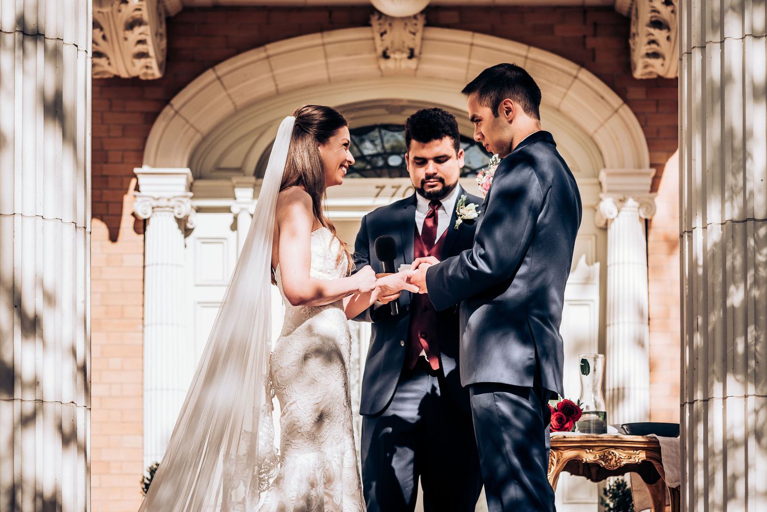 Wedding ceremony exchange of rings under historic archway with classical architecture.