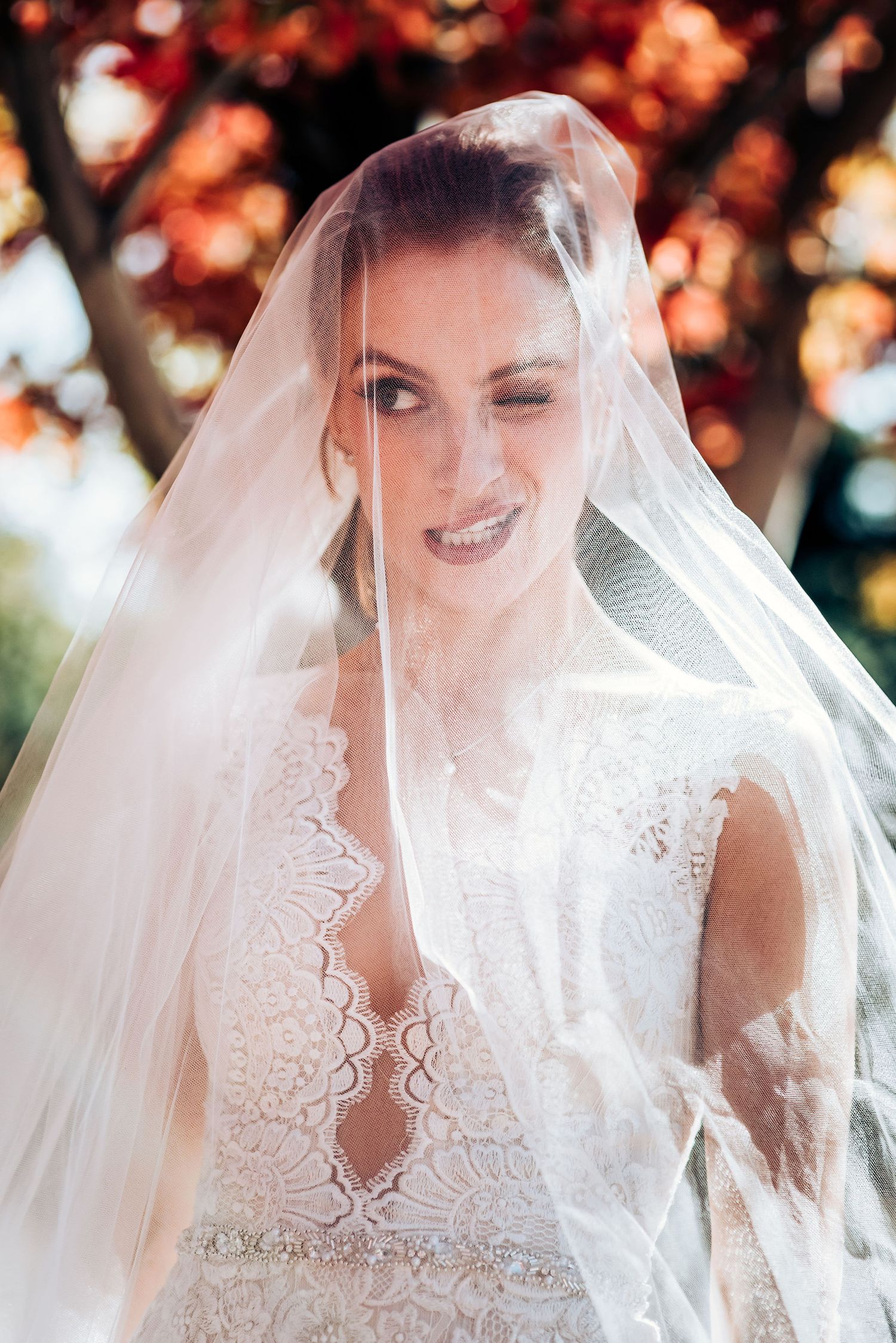 Ethereal bridal portrait with delicate lace veil against autumn red maple leaves.