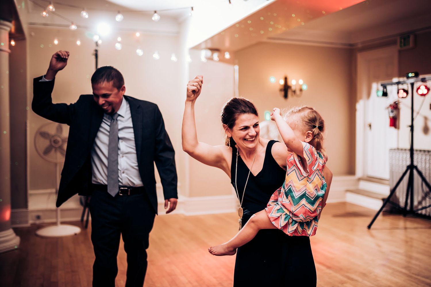 Party guests dancing and celebrating with raised arms on a wooden dance floor.