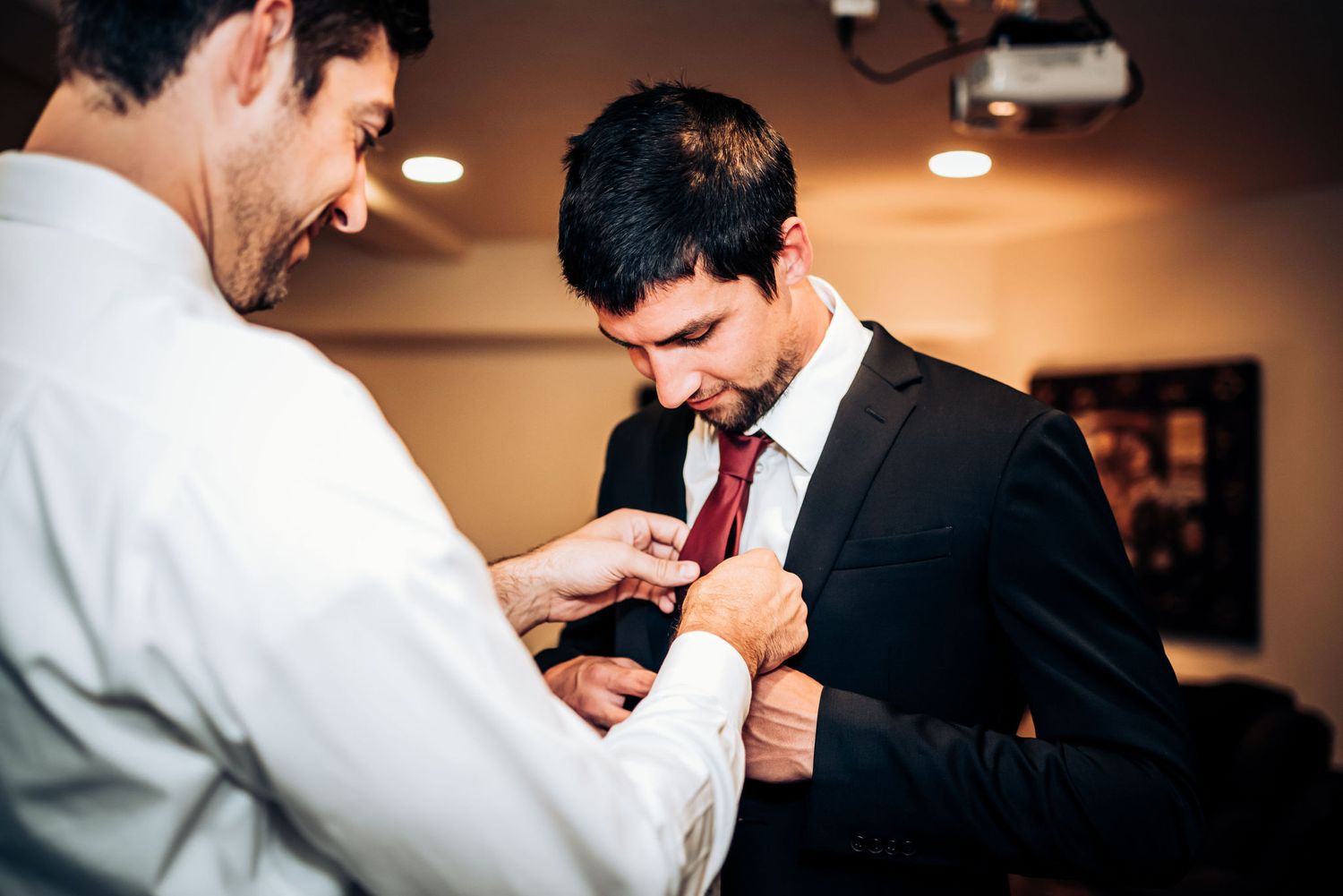 Two people helping with formal attire preparations before a wedding ceremony.