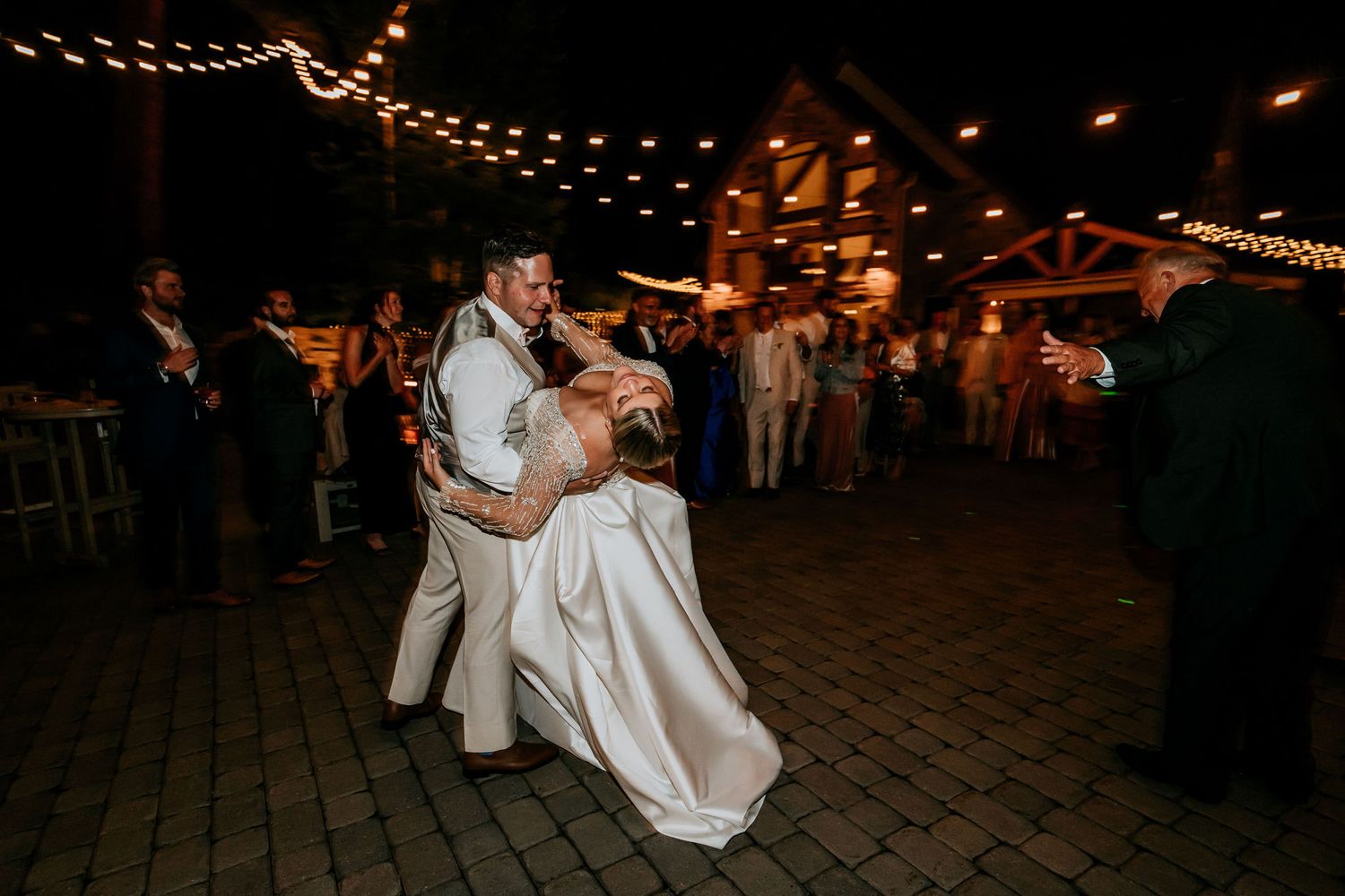 Couple dances on stone patio under string lights at night.