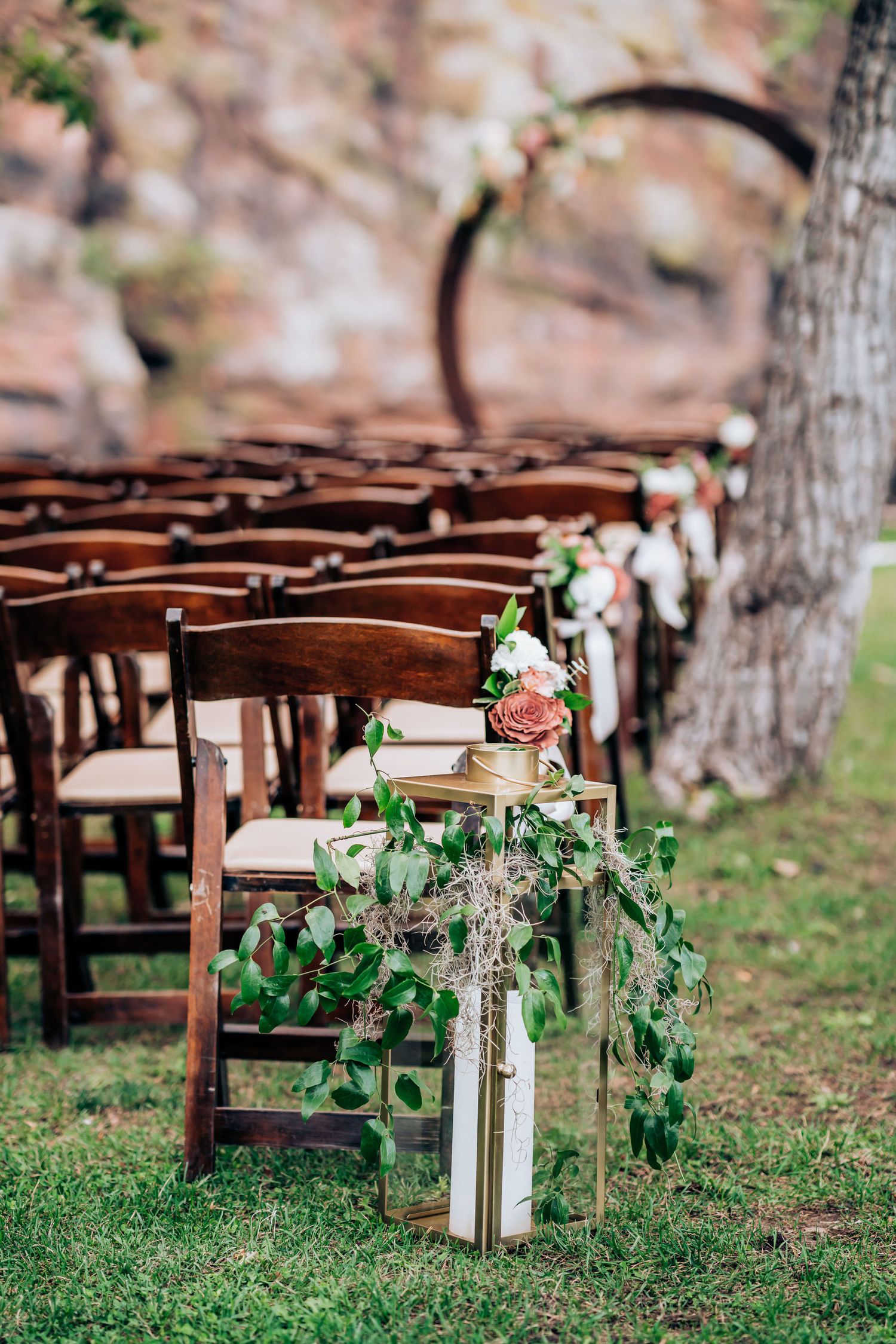 Wooden wedding ceremony chairs lined up with lantern and floral aisle decorations.