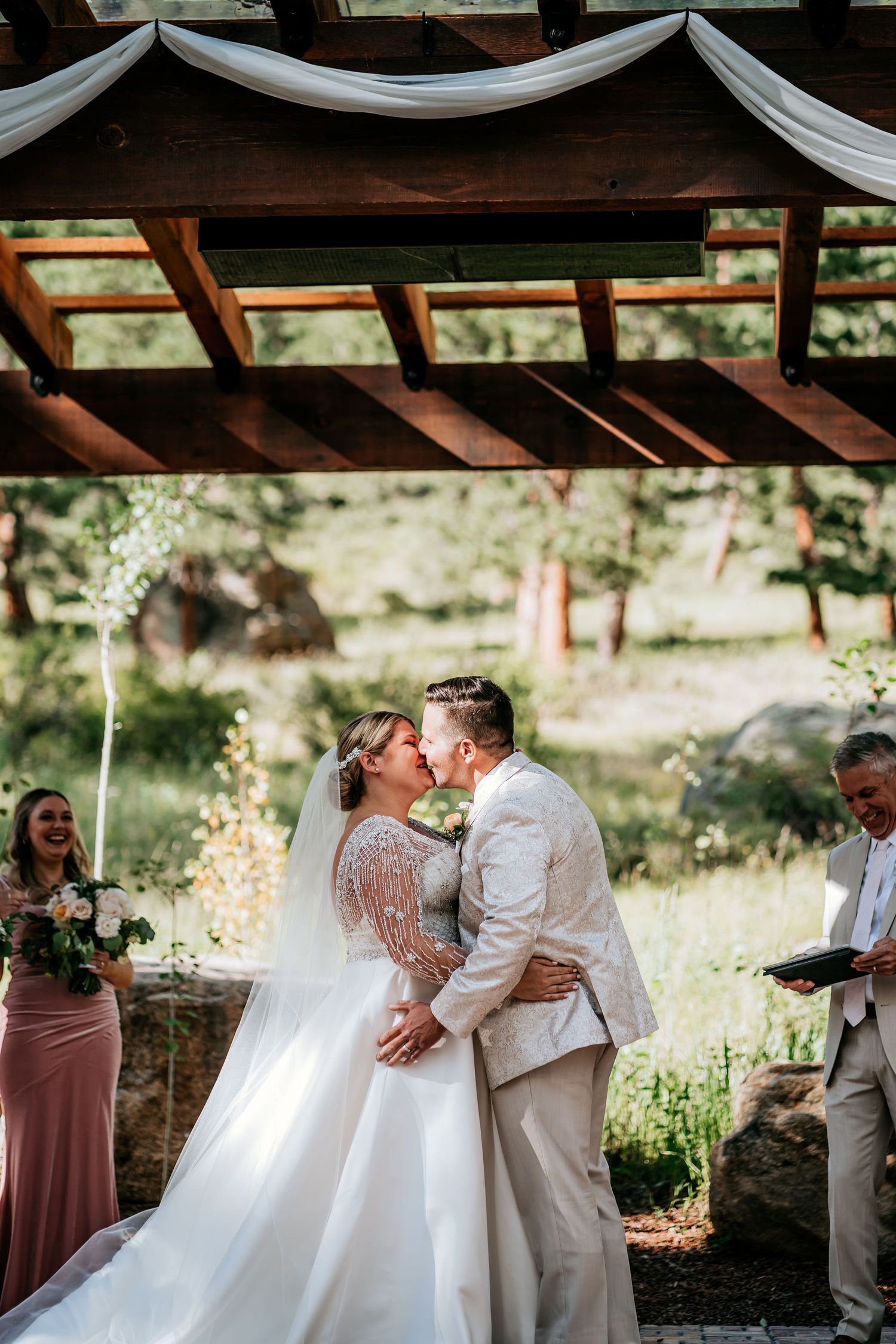 The newlyweds share their first kiss under a wooden pergola decorated with white draping.