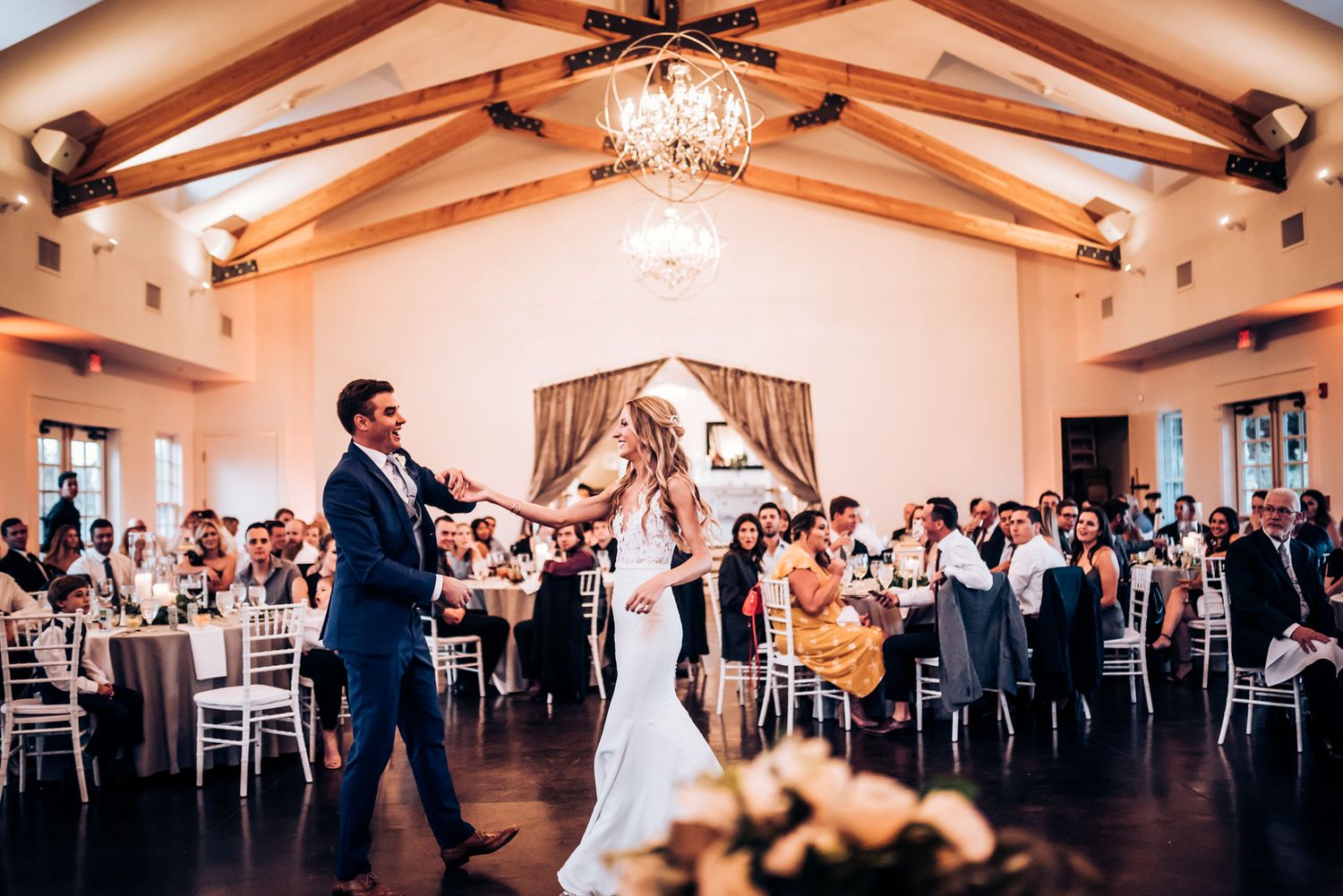 A couple dances in a grand reception hall with exposed wooden beams.
