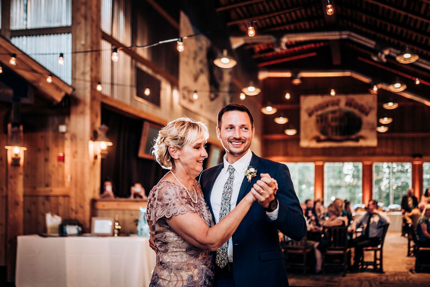 Elegant dance moment in wooden reception hall with warm lighting.