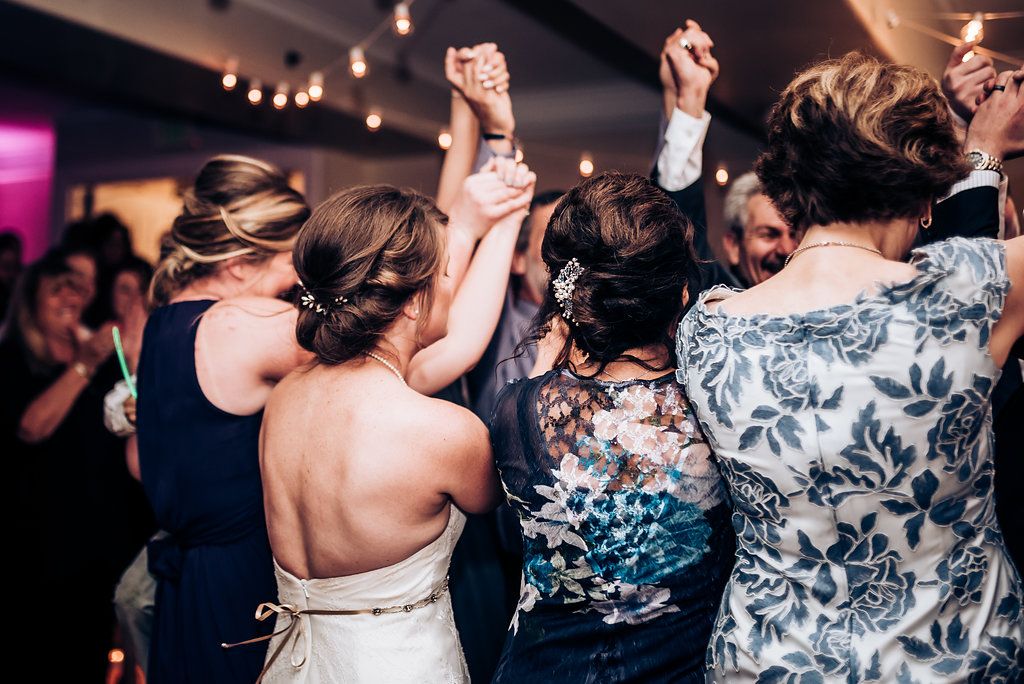 Guests dance with their arms raised during a wedding celebration with string lights overhead.
