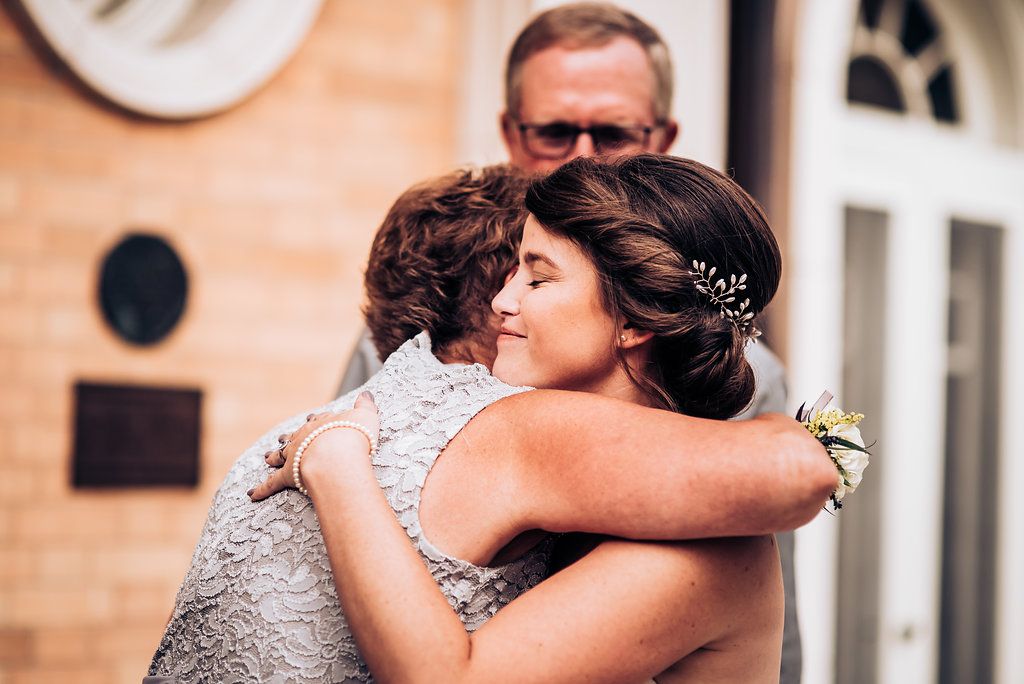 Two people share an emotional embrace at an elegant venue with a light-colored stone facade.