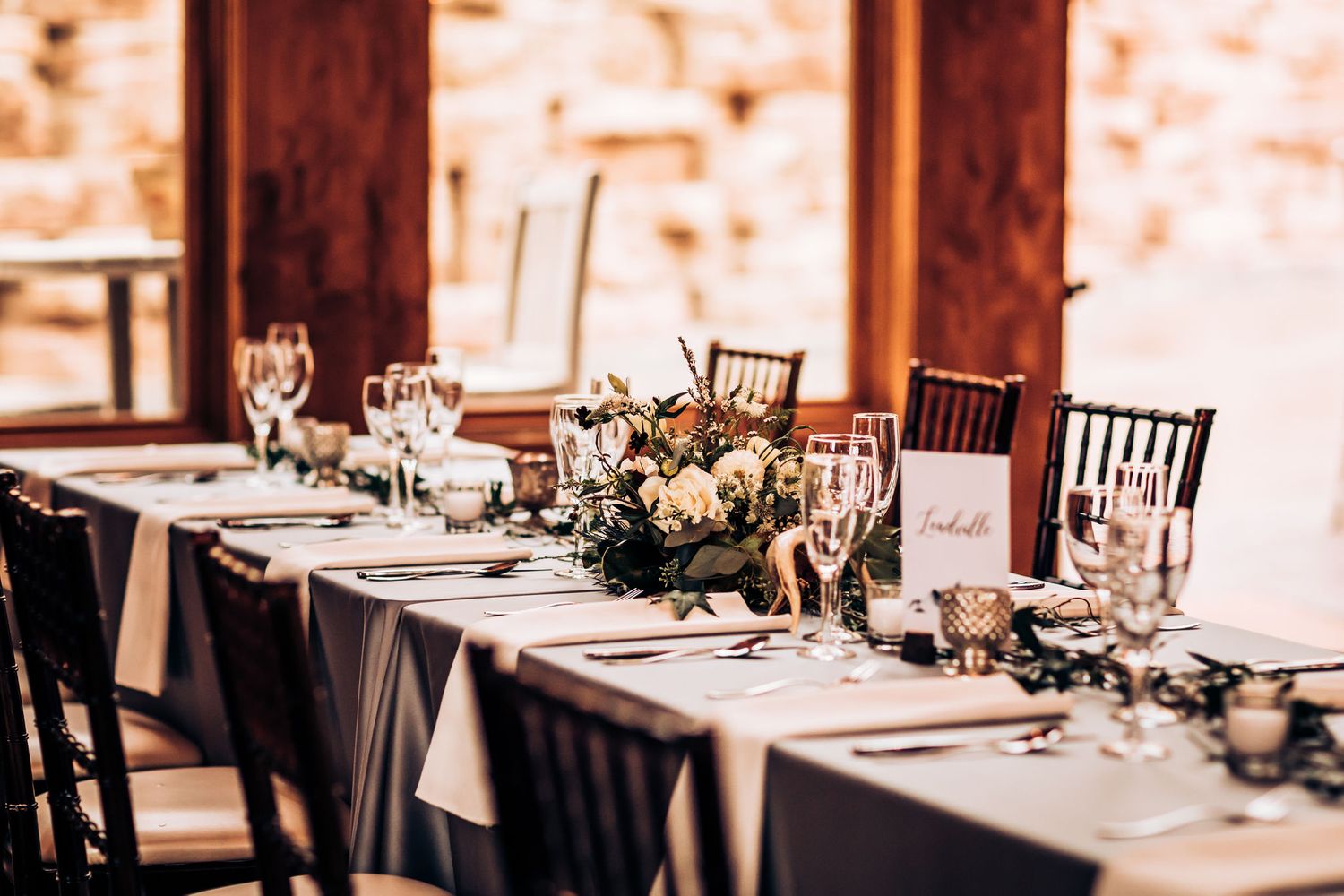 Elegant wedding reception table setting with dark chairs and floral centerpiece.