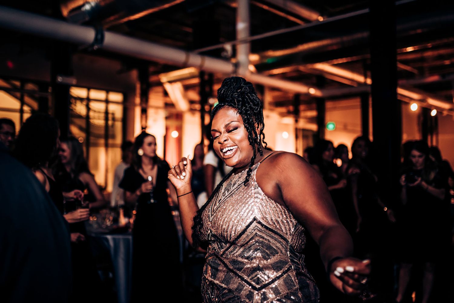 A guest dances joyfully in a sparkly dress at an evening wedding reception.