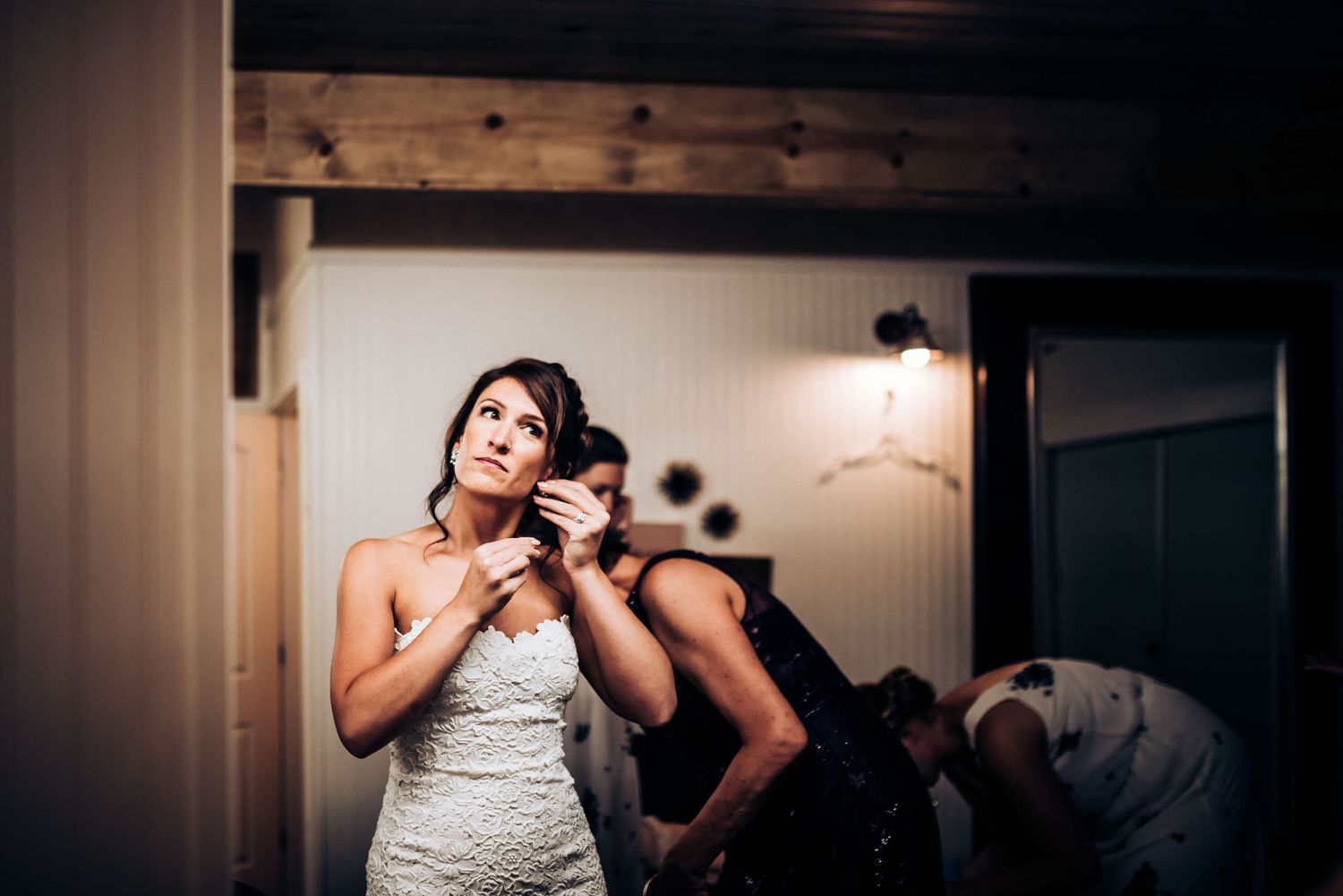 Bride putting on earrings while getting ready in rustic room.