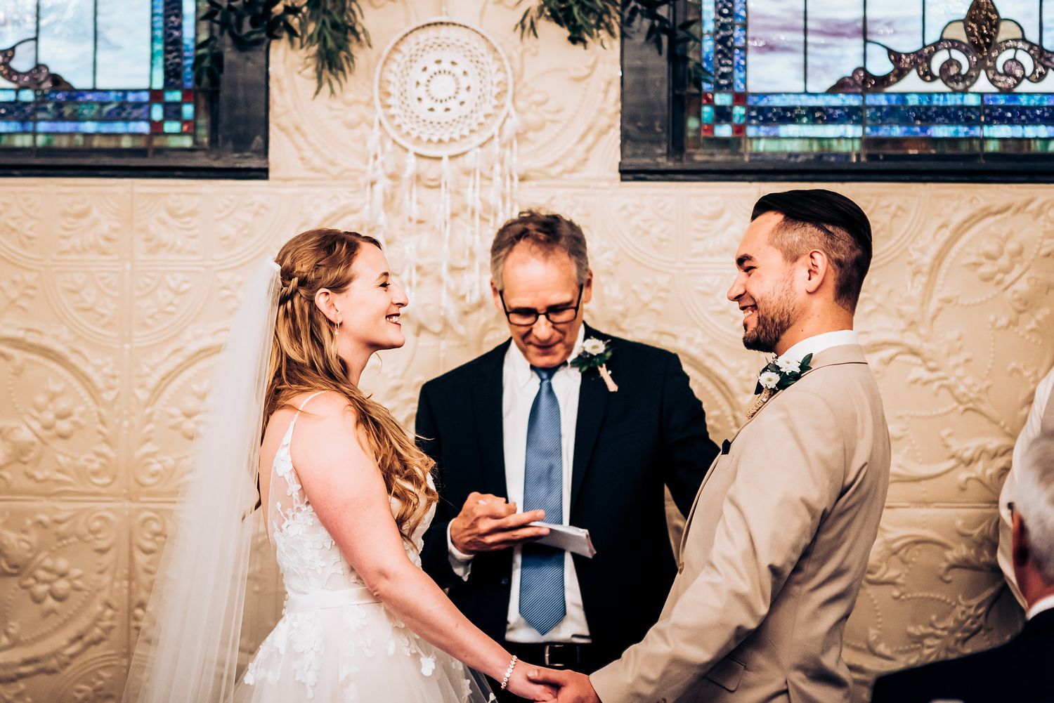 Wedding ceremony taking place under ornate wall decorations and stained glass windows.