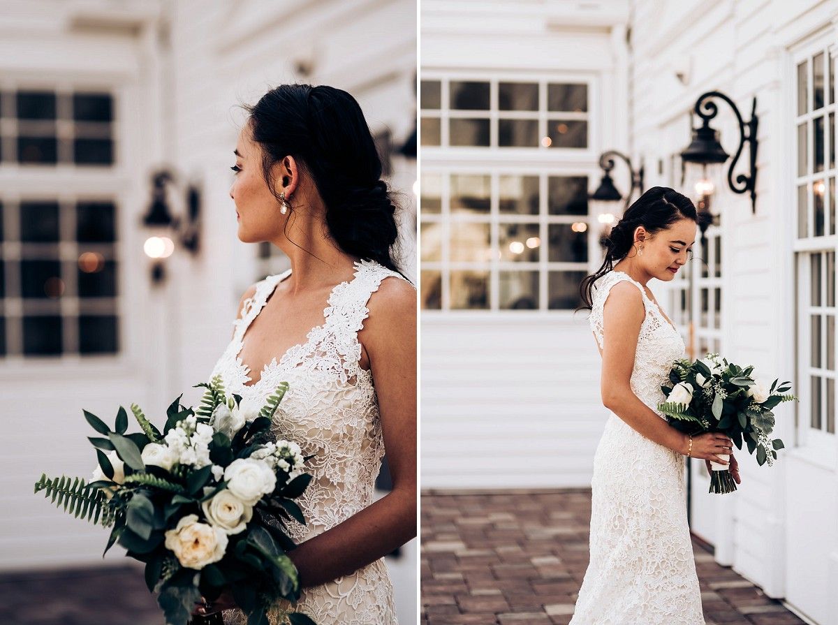Side views of bride in lace dress holding white and green bouquet against white building.