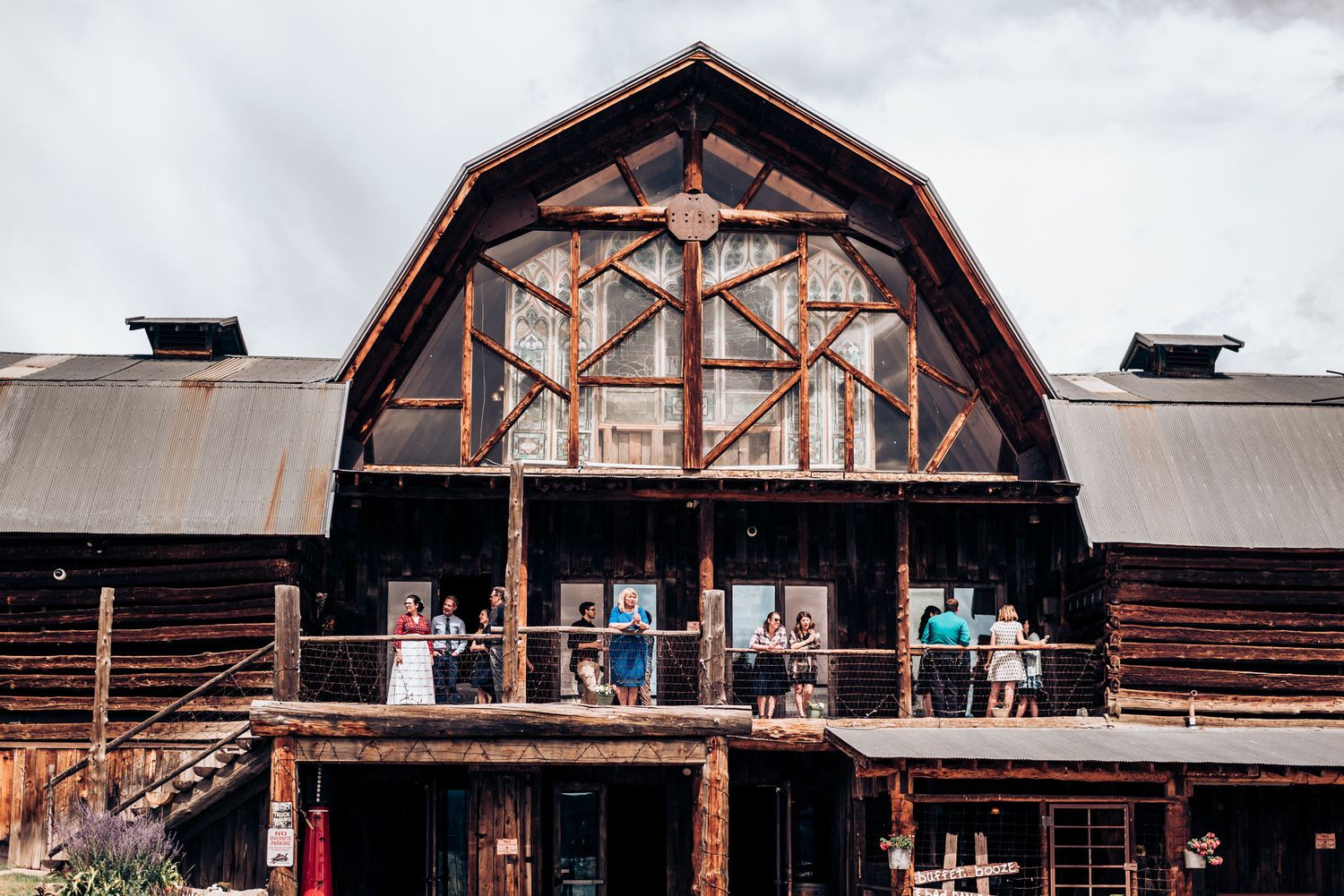 Wooden barn venue with distinctive arched architecture and wedding guests on balcony.