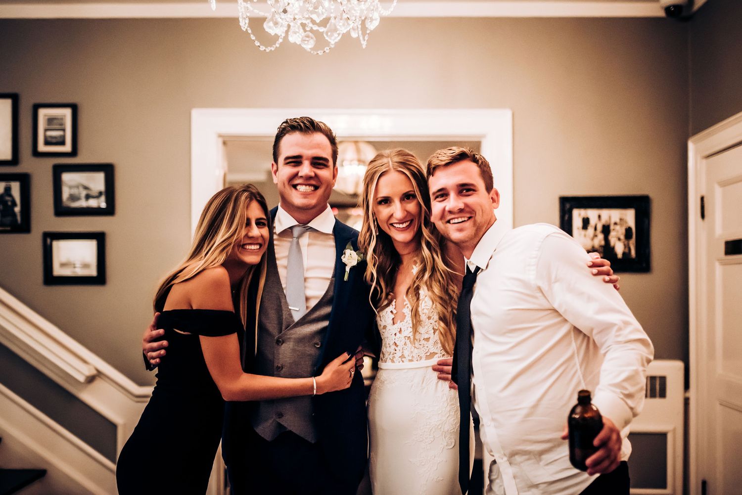 Four wedding attendees pose together for a joyful group photo under a chandelier.