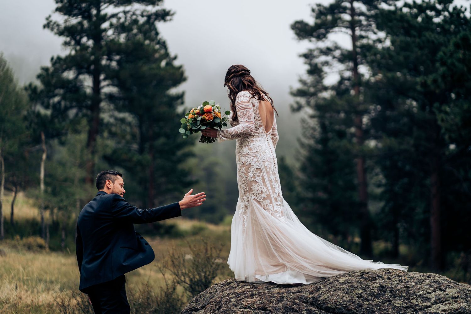 A couple shares a romantic moment on a rocky outcrop in the mountains during their wedding photoshoot.