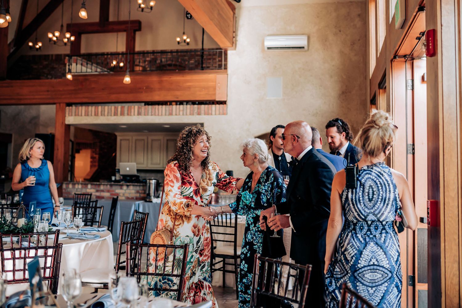 Wedding reception guests mingling in an elegant rustic venue with high ceilings.