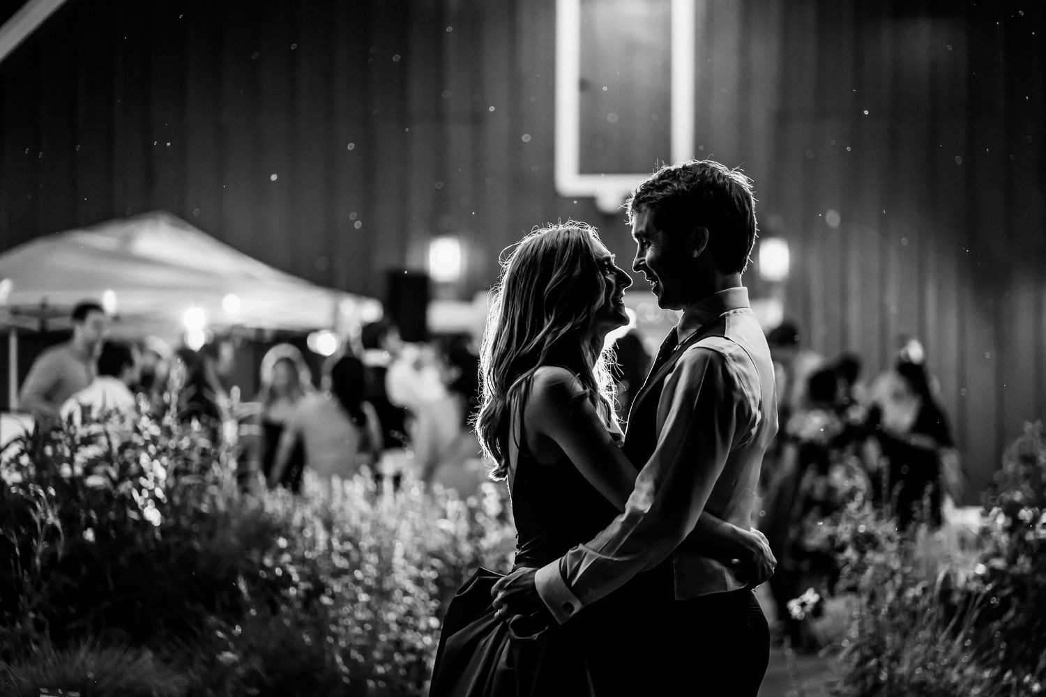 Romantic black and white portrait of couple embracing at nighttime garden reception.