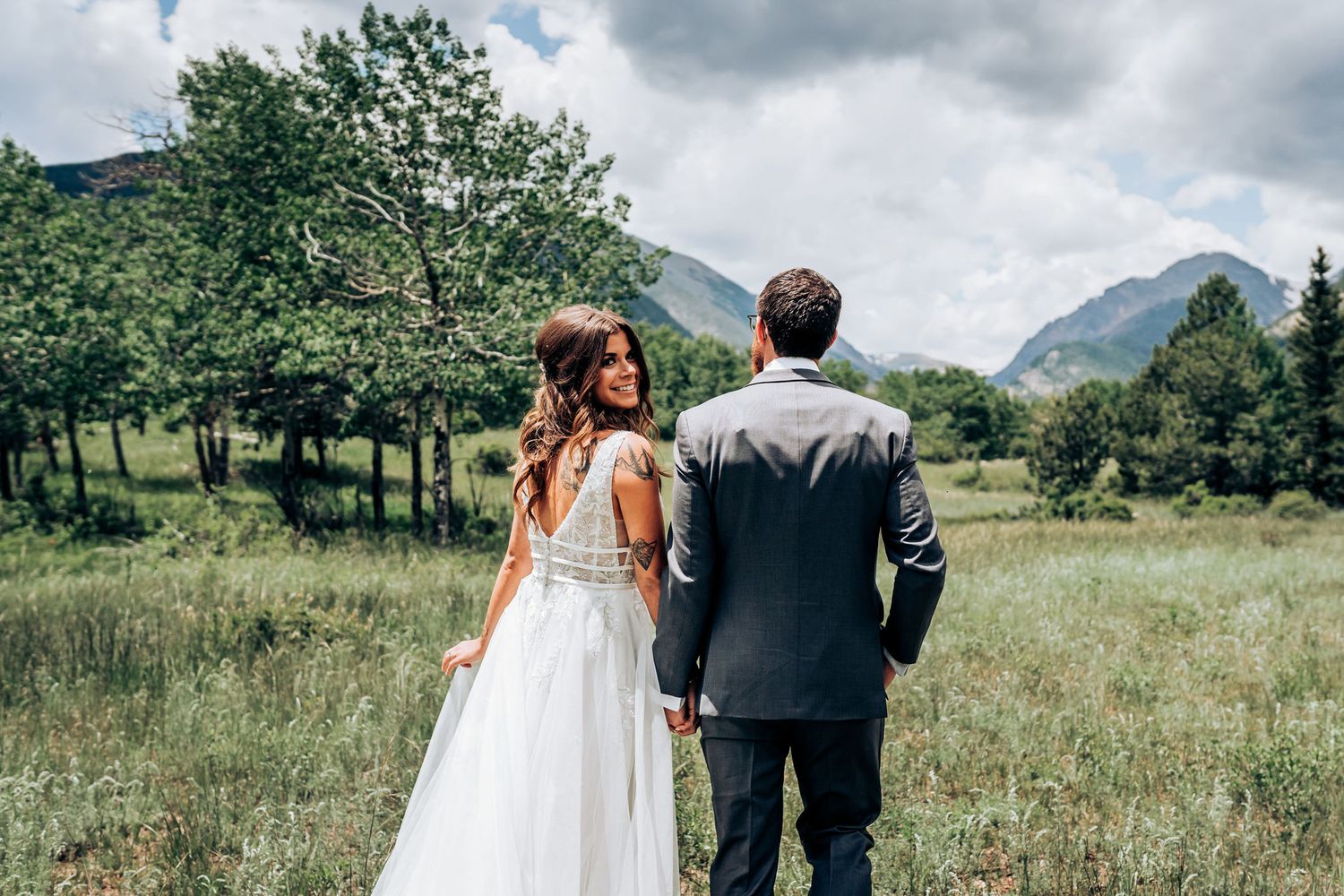 A wedding couple stands together looking at mountain vistas in a serene meadow.