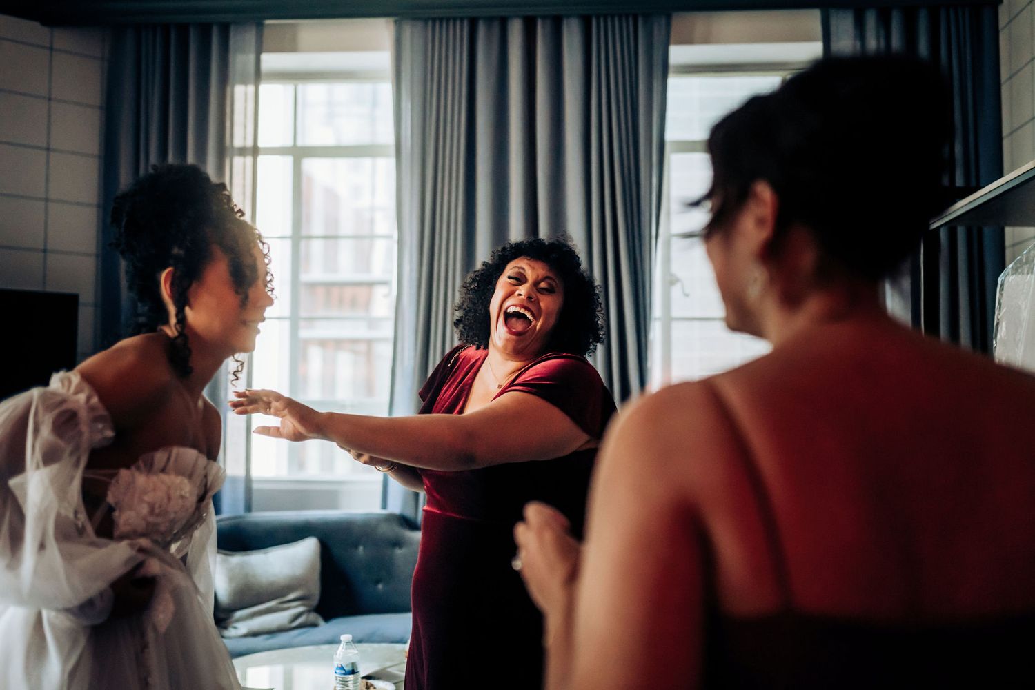 Wedding party members share laughter and excitement while getting ready in a hotel room.