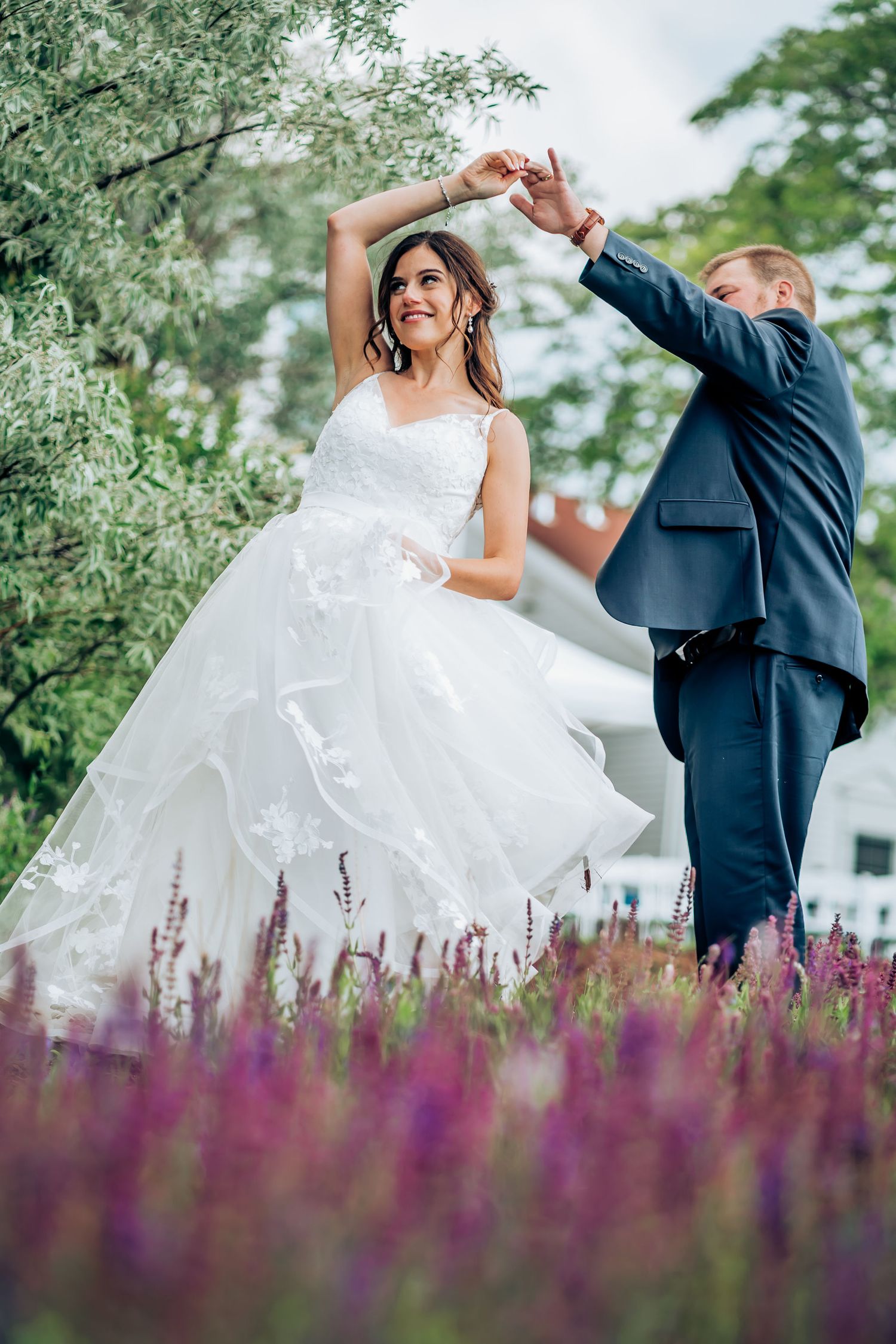 A joyful dance moment captured in a garden with blooming purple flowers in the foreground.