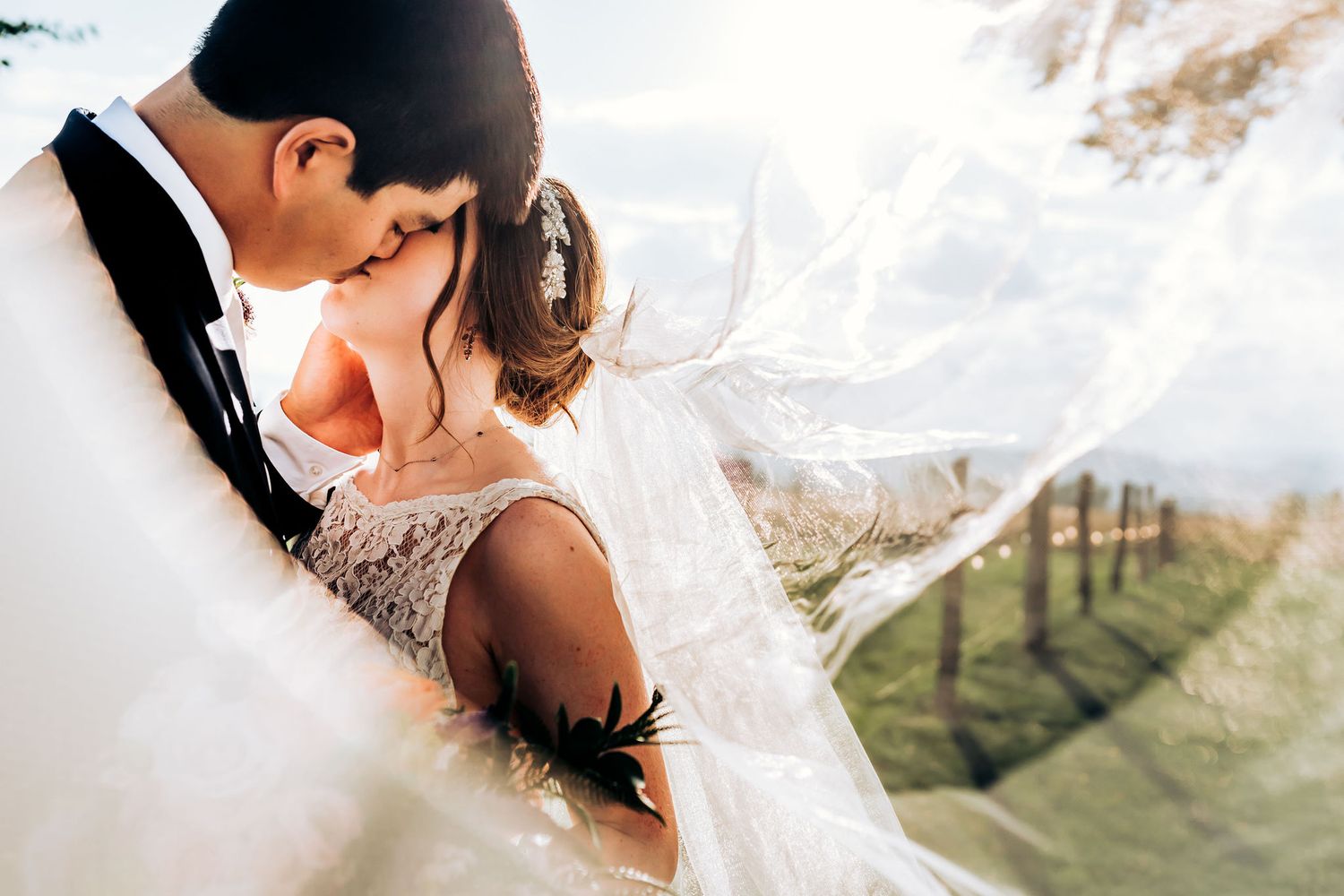 Intimate wedding moment captured through delicate veil with rolling hills in background.