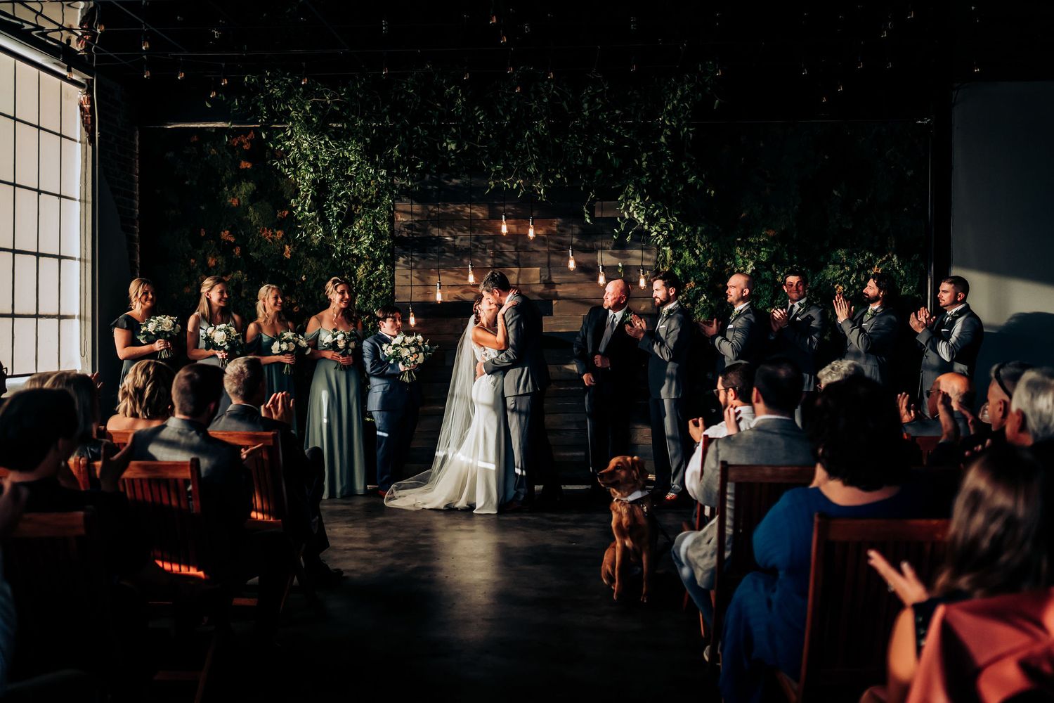 Wedding ceremony in dark venue with string lights and guests watching from wooden chairs.