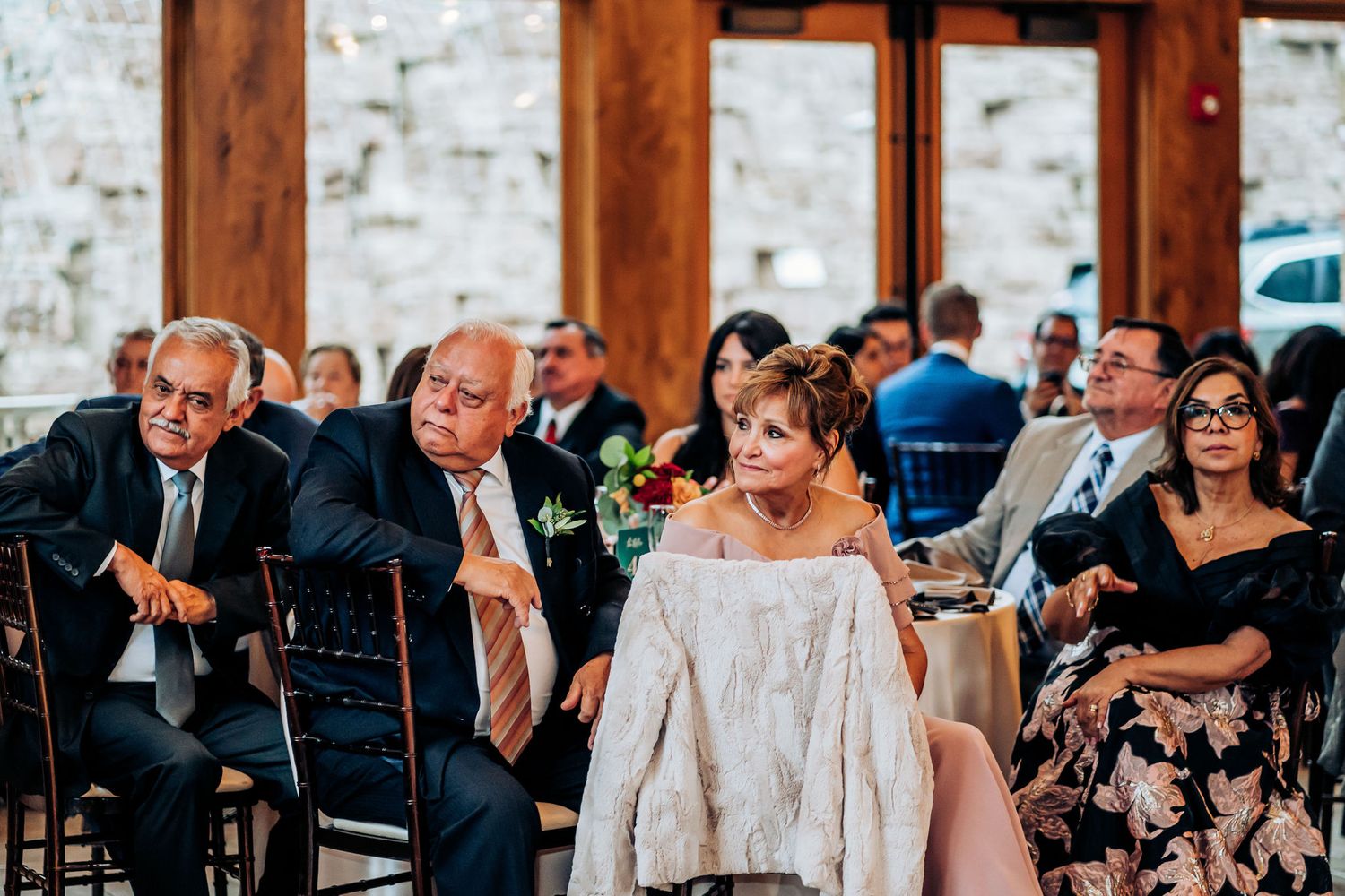Wedding guests seated at tables in a rustic venue with exposed wooden beams.