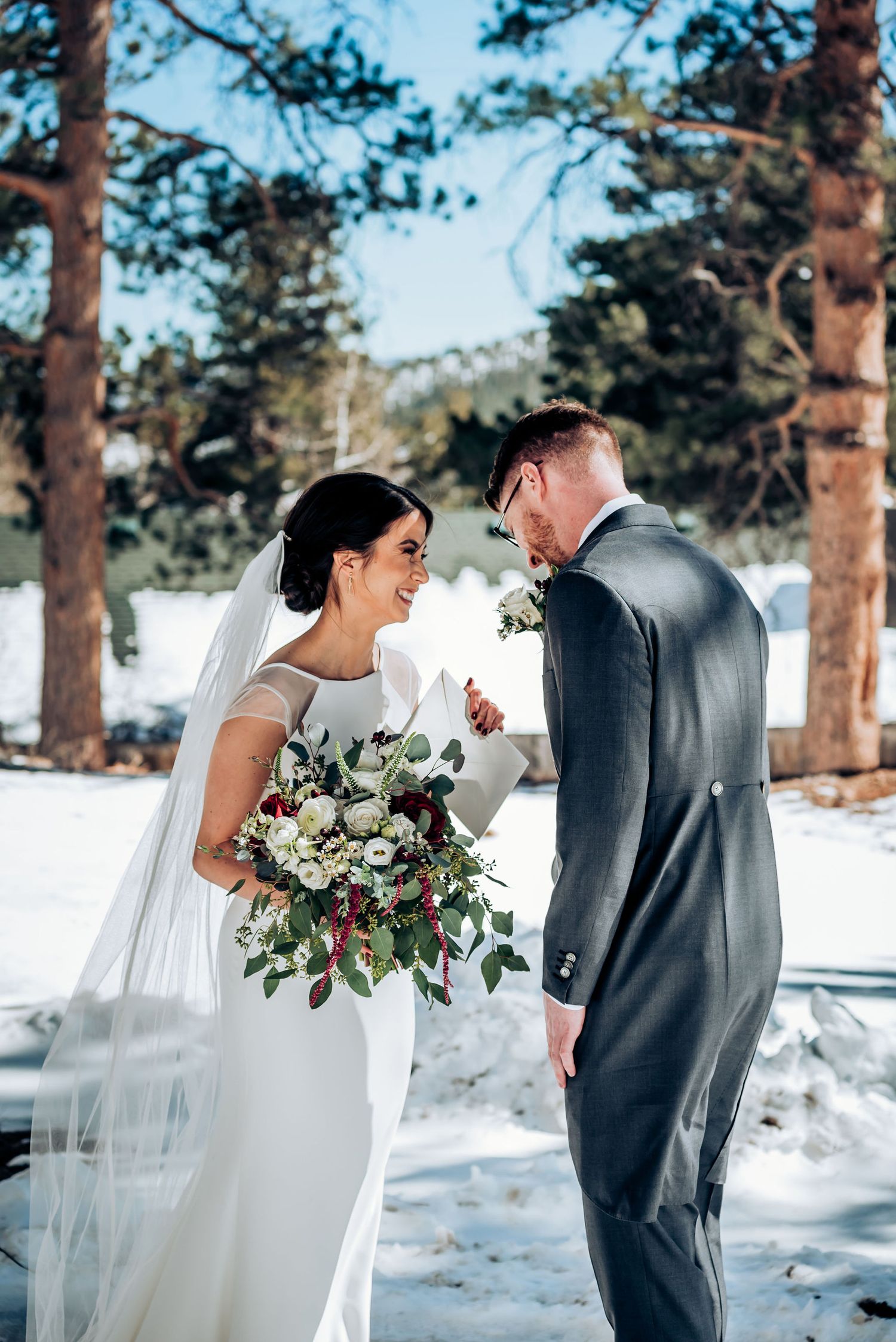 A joyful wedding moment between newlyweds surrounded by snow and pine trees.