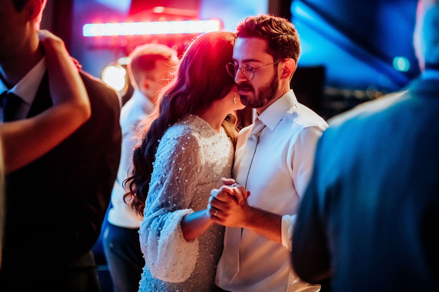 Intimate dance moment at wedding reception with red neon lighting in background.