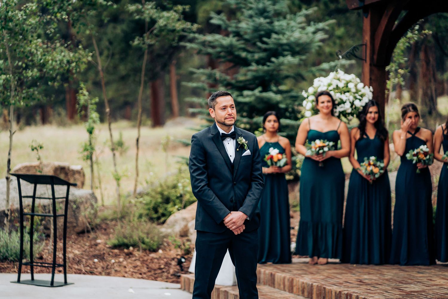 Wedding party assembled on a stone patio with navy bridesmaids dresses and white floral bouquets.