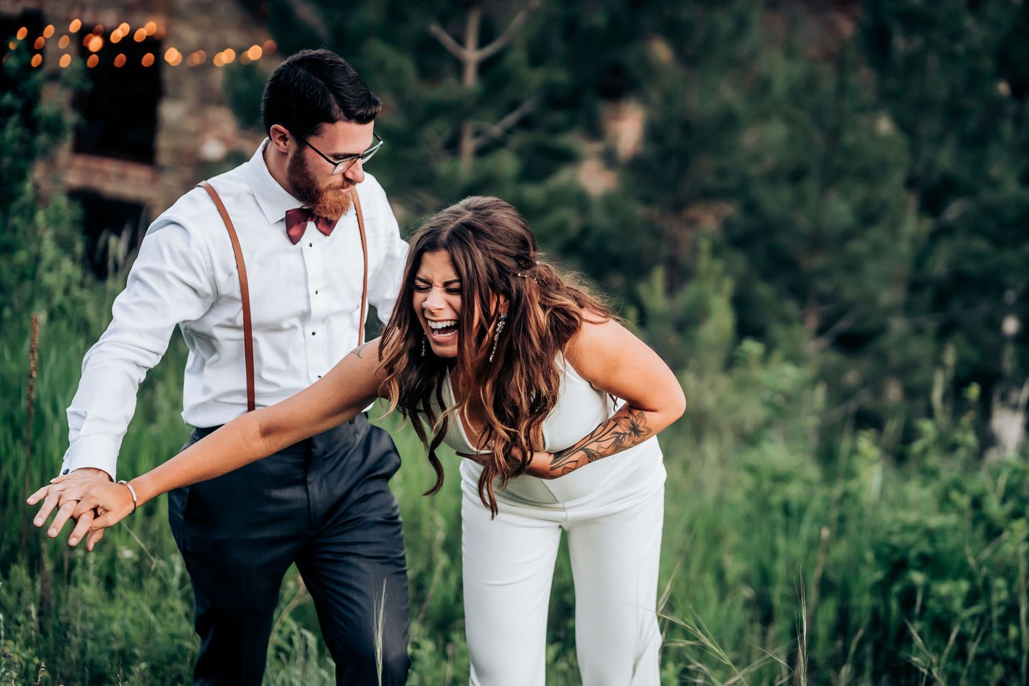 Dancing couple in white and dark attire moving through mountain meadow at sunset.