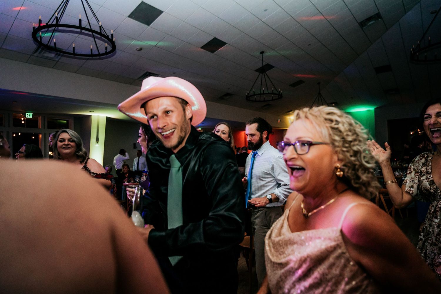 Man in pink cowboy hat laughing with woman in pink dress at festive wedding reception.