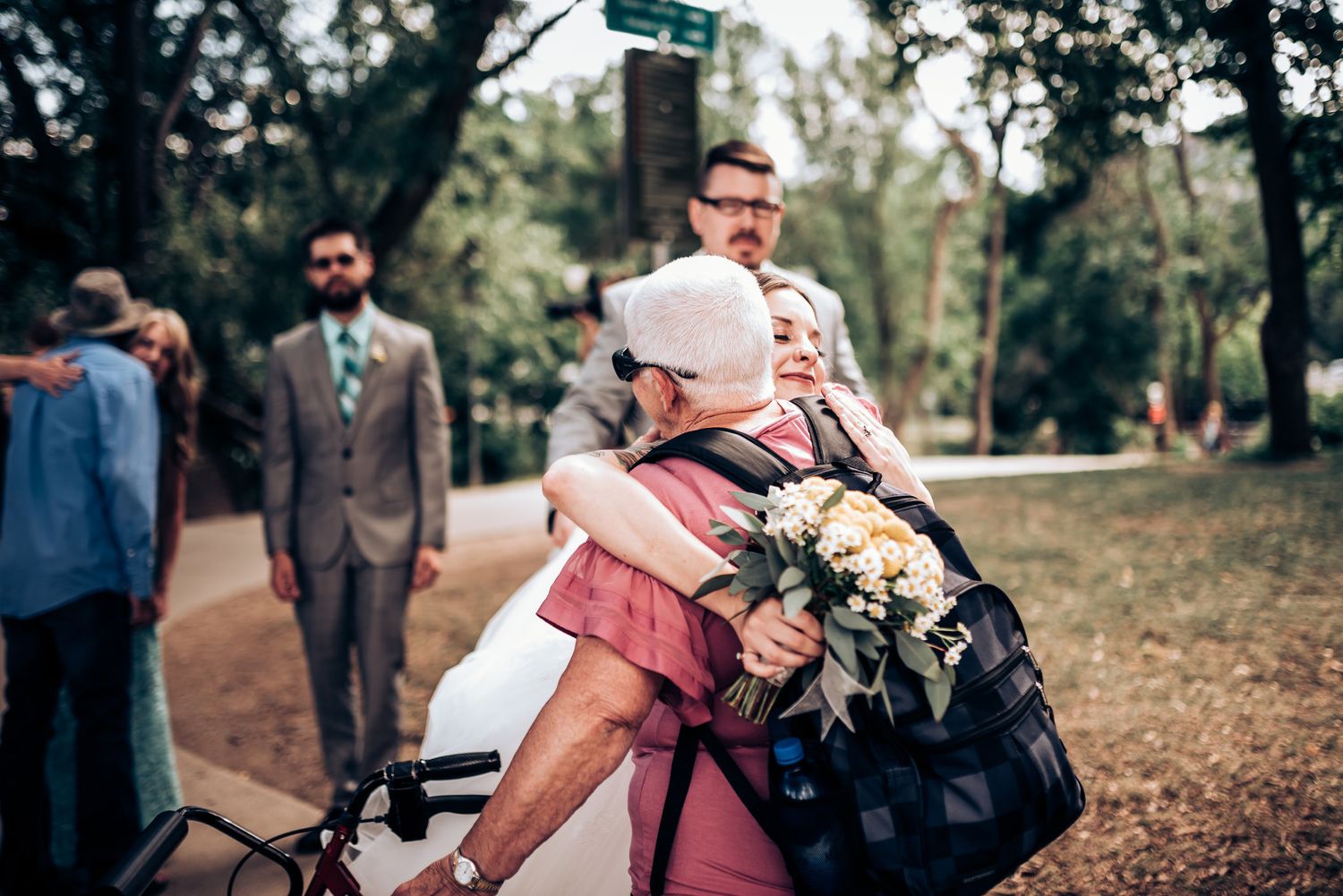 An emotional embrace between wedding party members in an outdoor garden setting.