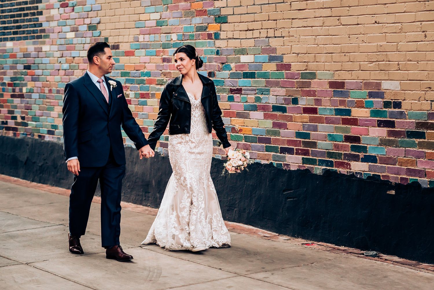 Wedding couple posing against colorful brick wall in urban setting.