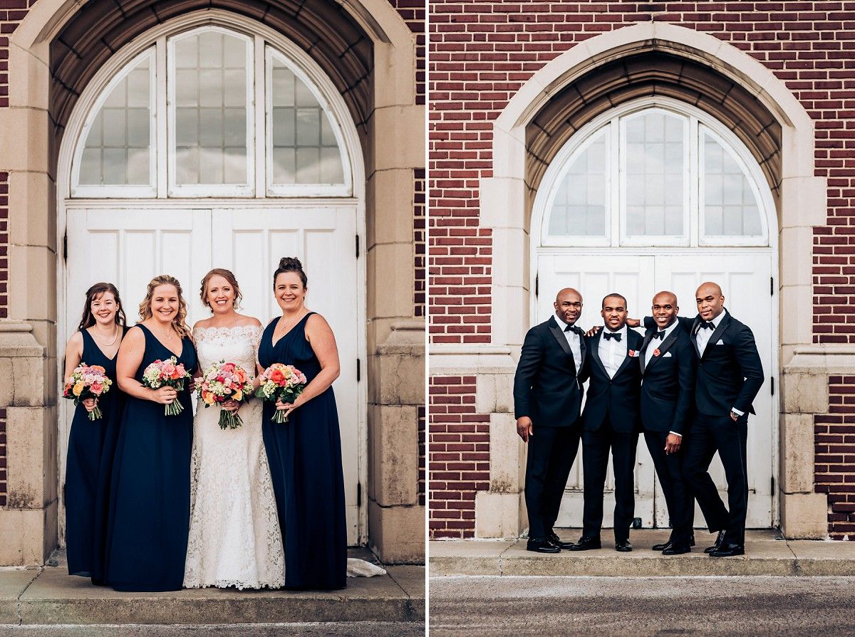 Wedding party in navy blue and formal attire pose in front of arched church windows and brick walls.