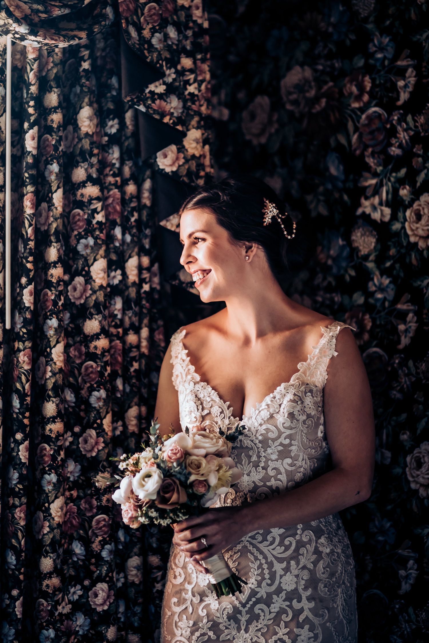 Classical bridal portrait with a delicate bouquet against dark floral wallpaper.