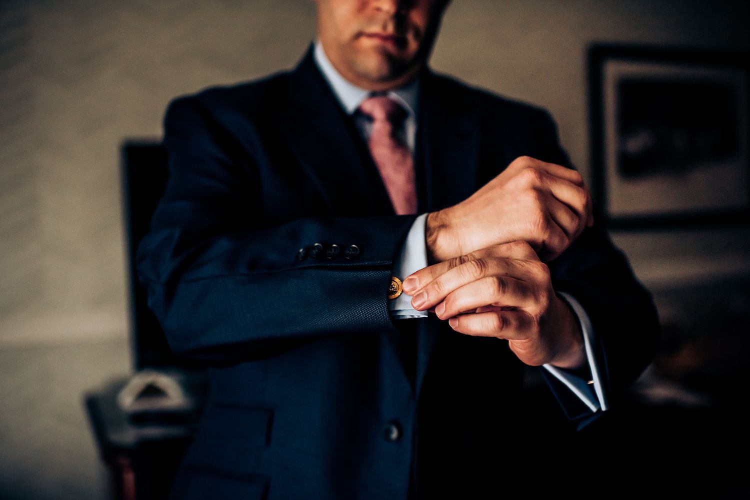 Professional in a dark suit and pink tie adjusts his sleeve cuff.