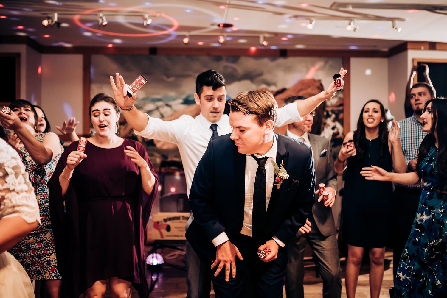 Wedding guests dancing enthusiastically on a reception dance floor under ambient lighting.