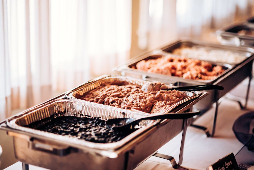 Three metal chafing dishes in a row containing different hot food items at a catering setup.