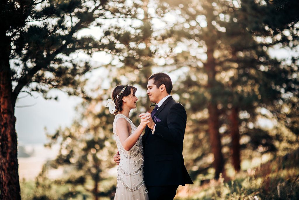 A romantic wedding moment captured between a couple dancing among tall pine trees at sunset.