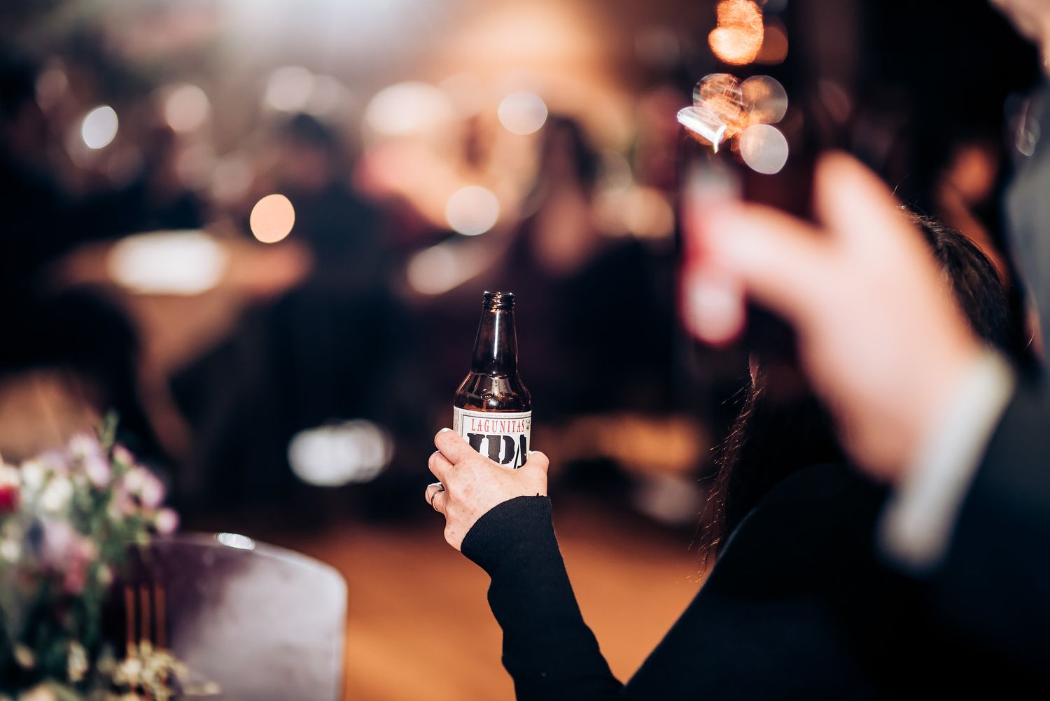 A guest raises a bottle in celebration during a dimly lit wedding reception.