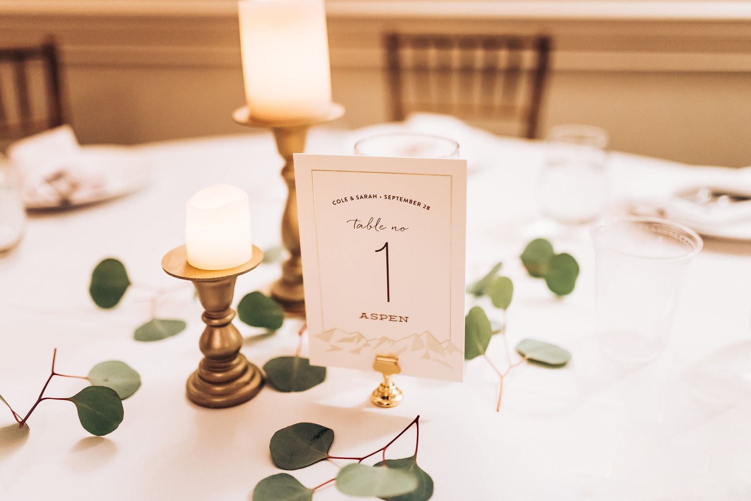 Elegant wedding table setting with candles, eucalyptus leaves and table number card.