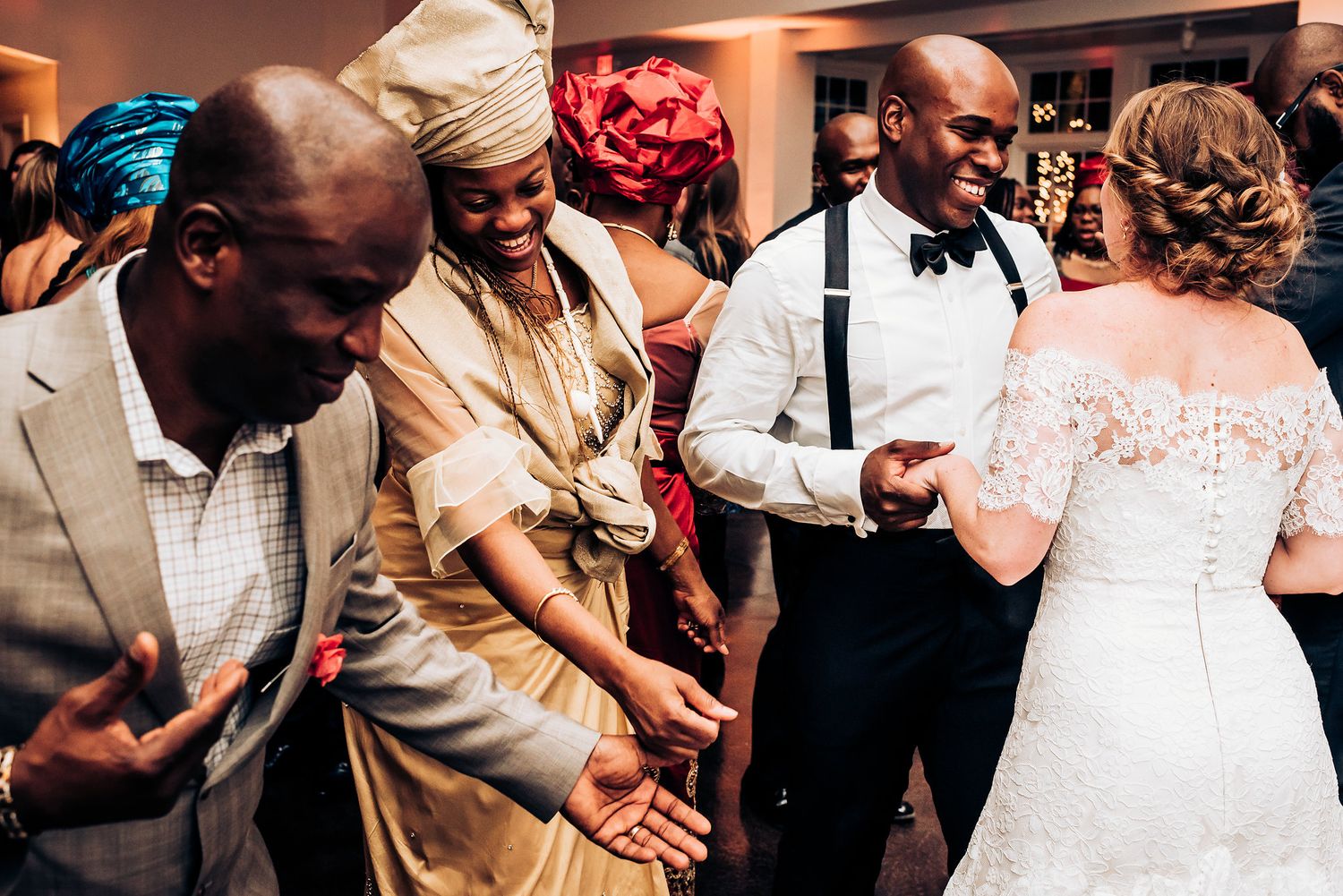 Wedding guests dance enthusiastically on the reception dance floor in an indoor venue.
