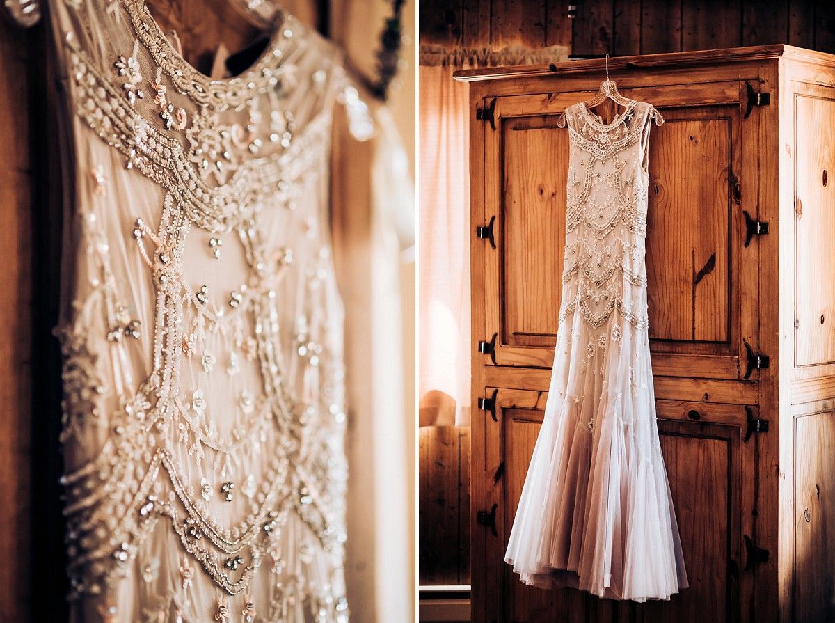 Detailed beaded wedding dress hangs elegantly against rustic wooden doors.